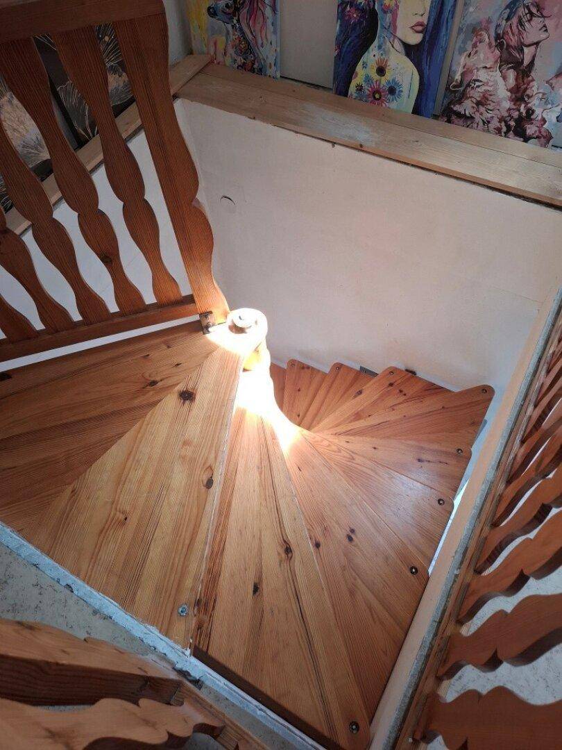 Wendeltreppe aus hellem Holz mit geschnitzten Geländern, die in ein Obergeschoss führt.