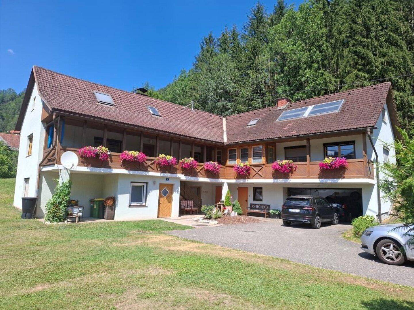 Großes Wohnhaus mit mehreren Balkonen, Garagenzufahrt und einem gepflegten Vorgarten.
