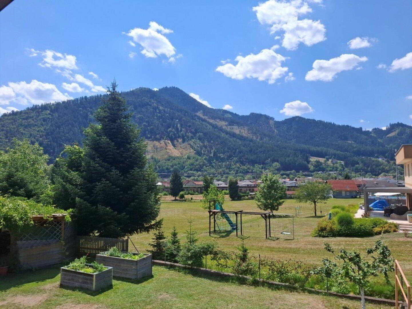 Großer Garten mit Spielplatz, Hochbeeten und weitem Blick auf die umliegende Berglandschaft.