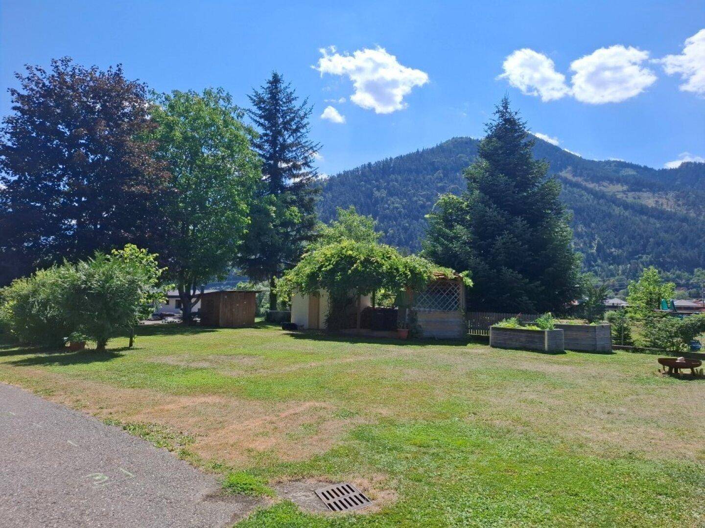 Weitläufiger Garten mit Rasen, Bäumen, einem Gartenhaus und Blick auf die Berge.