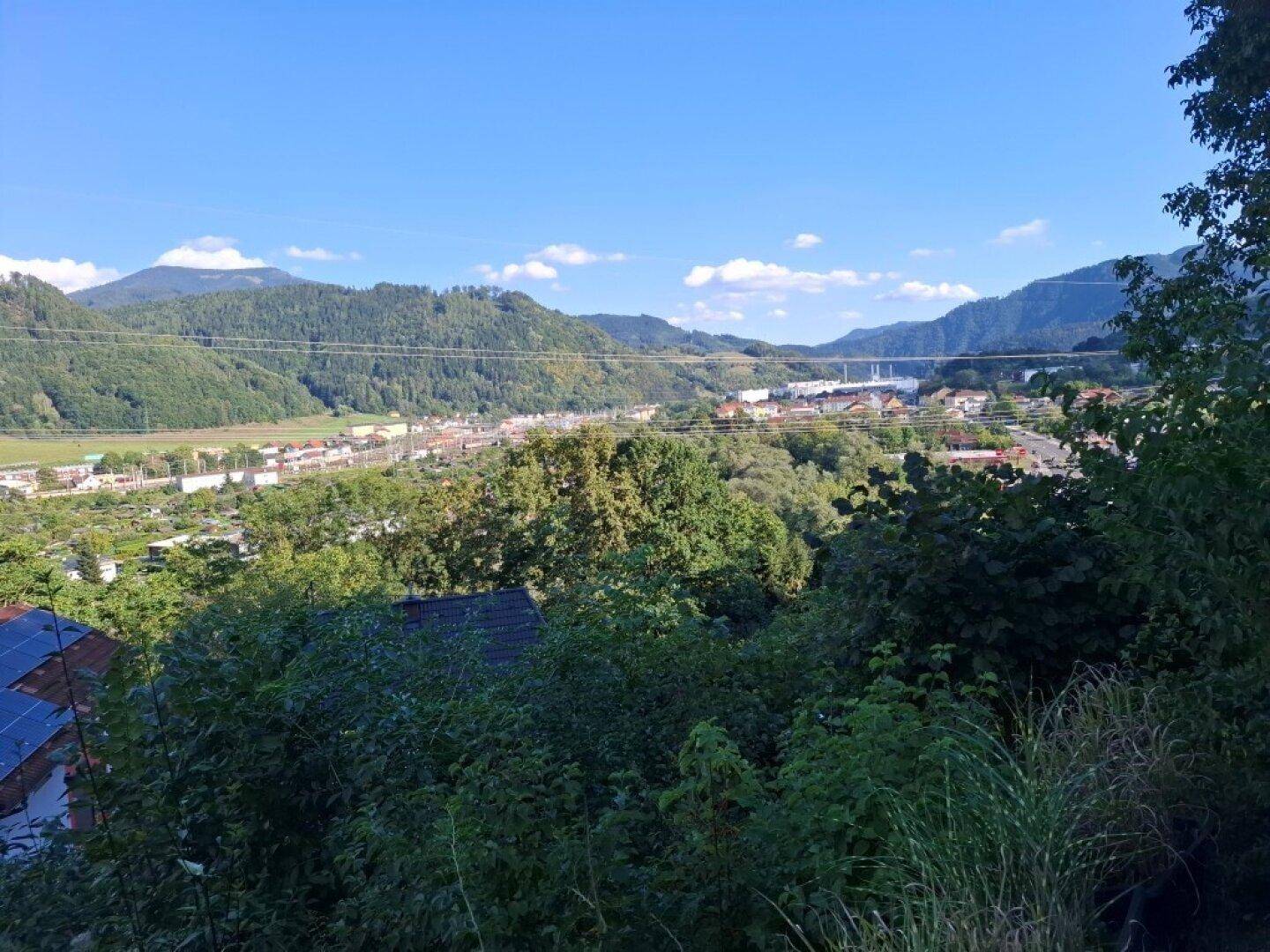 Panoramablick über ein grünes Tal mit Bergen und einer Siedlung in der Ferne.