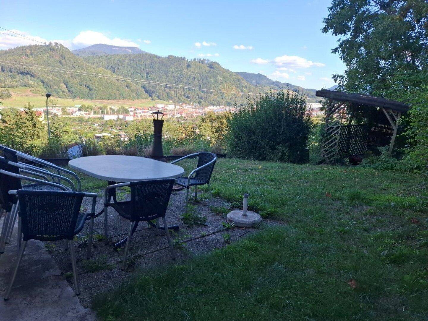 Gemütlicher Sitzbereich im Garten mit Esstisch und Stühlen, bietet einen weiten Blick ins Tal.