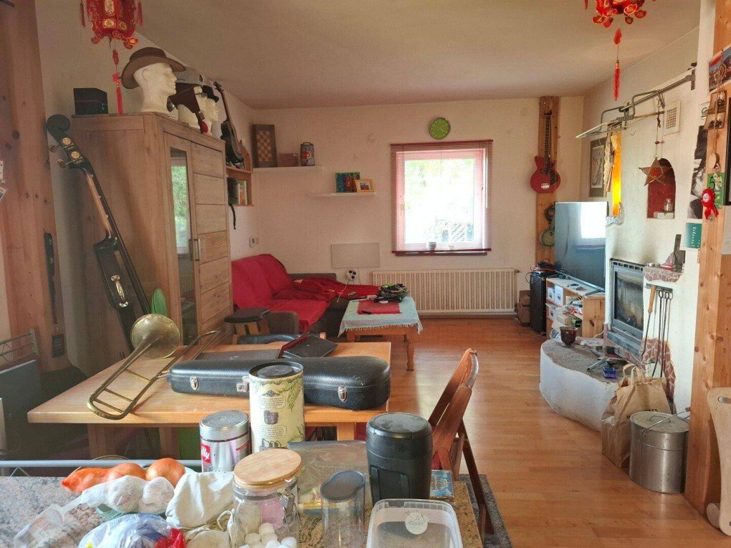 Wohnzimmer mit Holzboden, Fenster und vielfältiger Einrichtung, darunter Musikinstrumente.