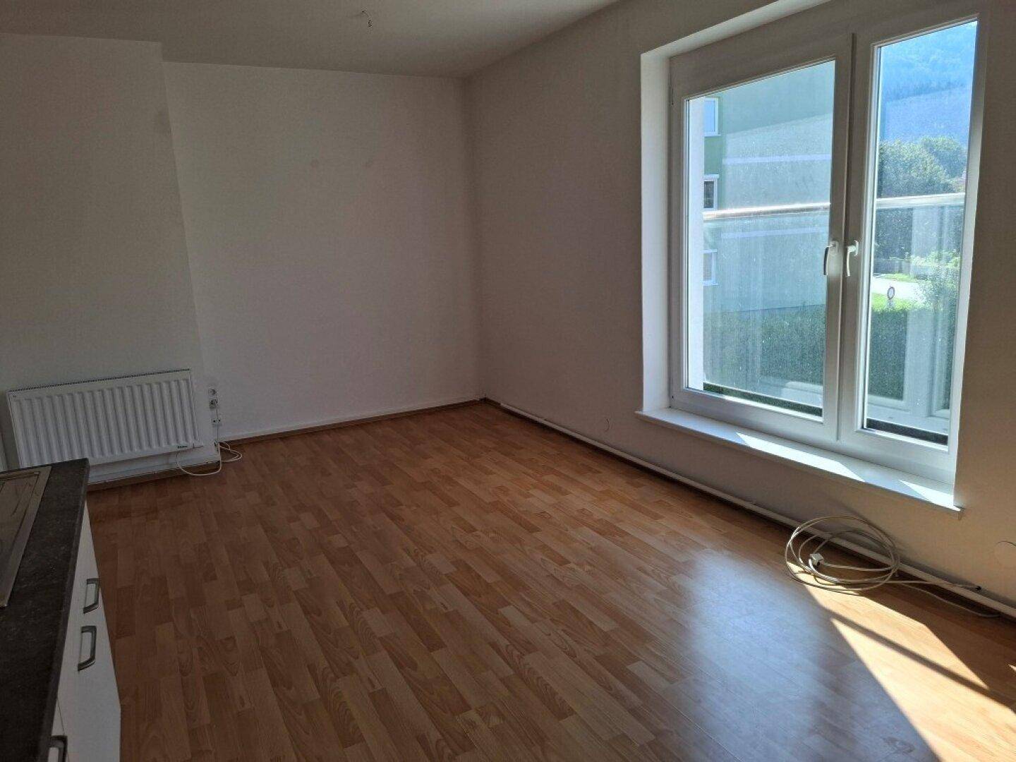 Geräumiger Wohnbereich mit Laminatboden, großem Fenster und Heizkörper, bereit zur individuellen Gestaltung.