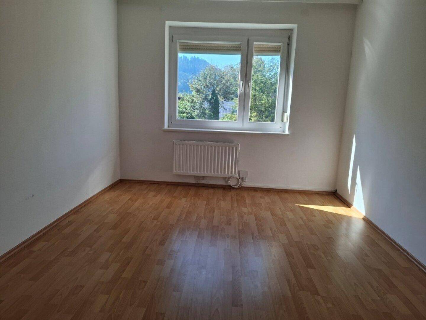 Helles Schlafzimmer mit Laminatboden, großem Fenster und Heizkörper, ideal für Ruhe und Entspannung.