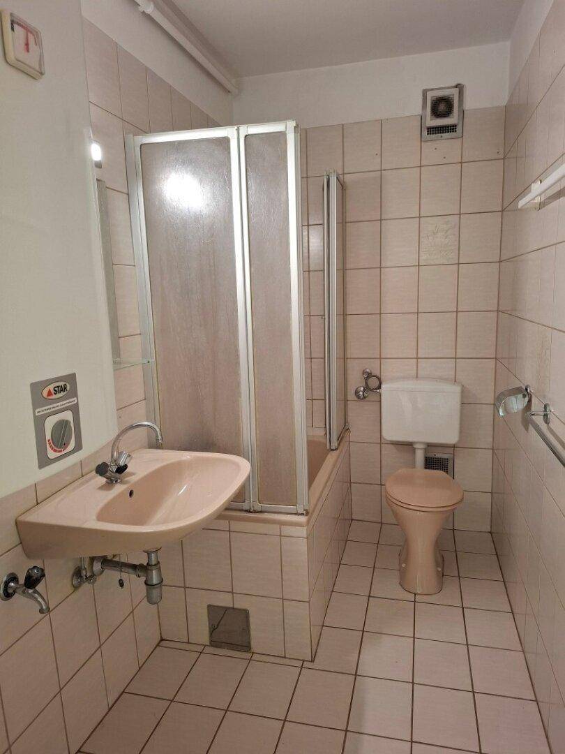 Badezimmer mit Badewanne, Duschabtrennung, Waschbecken und WC, ausgestattet mit beigefarbenen Fliesen.