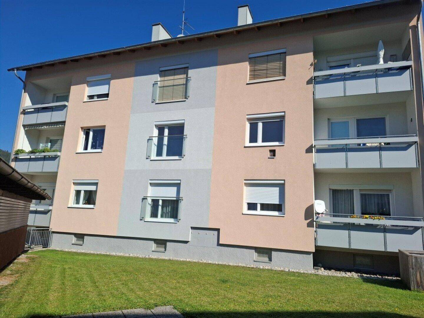 Mehrfamilienhaus mit mehreren Balkonen und einer gepflegten Rasenfläche im Vordergrund.
