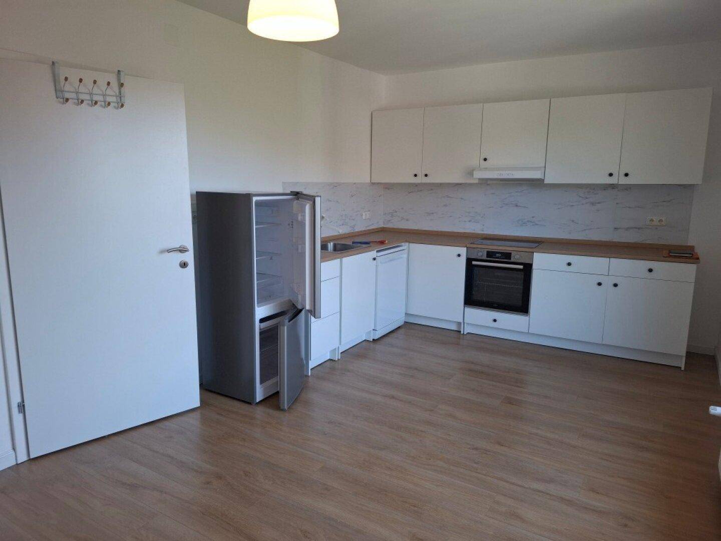 Funktionale Küche mit weißen Schränken, Holzarbeitsplatte und einem freistehenden Kühlschrank.