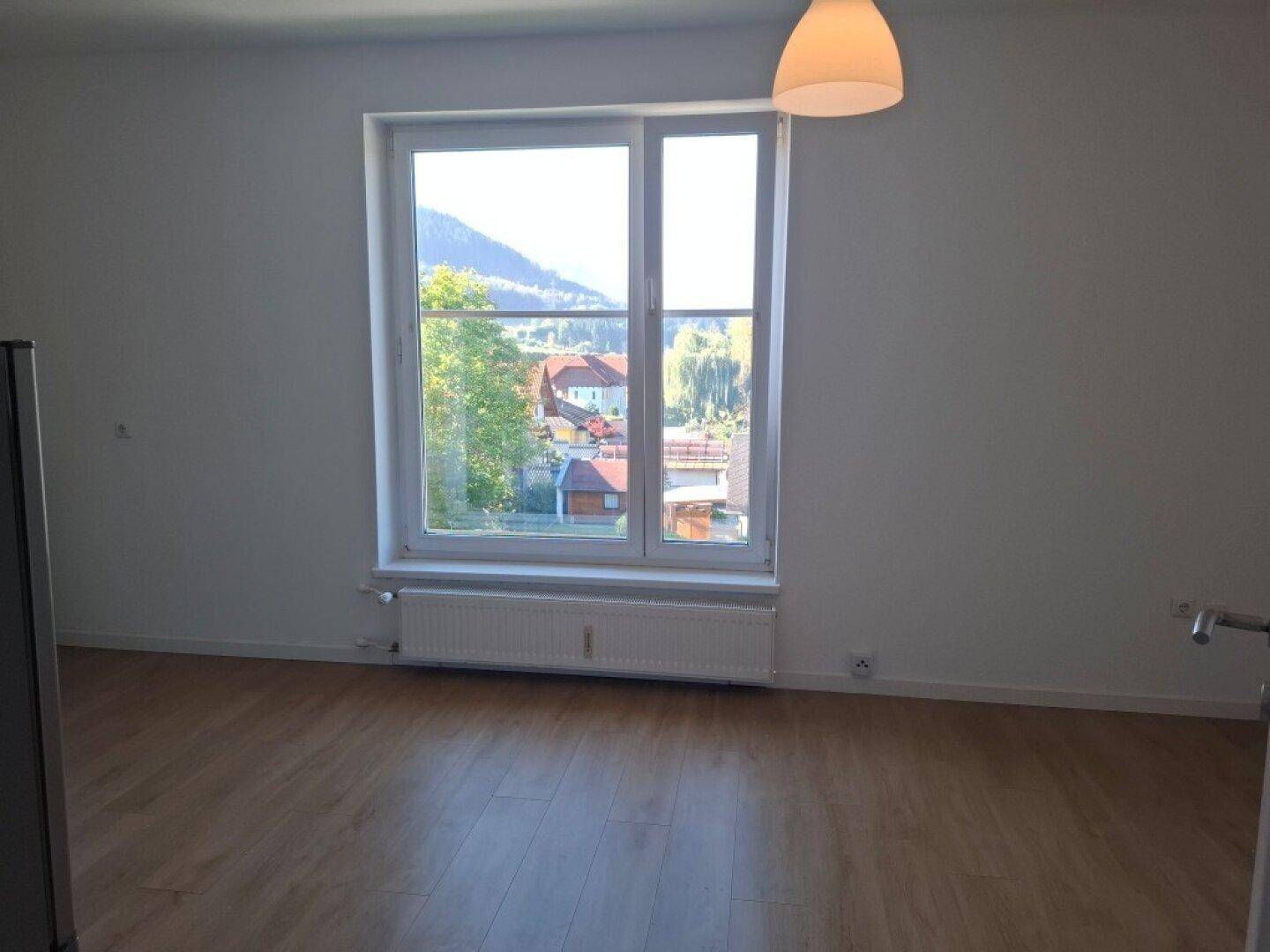 Lichtdurchfluteter Wohnbereich mit großem Fenster und Panoramablick auf die umliegende Natur und Berge.
