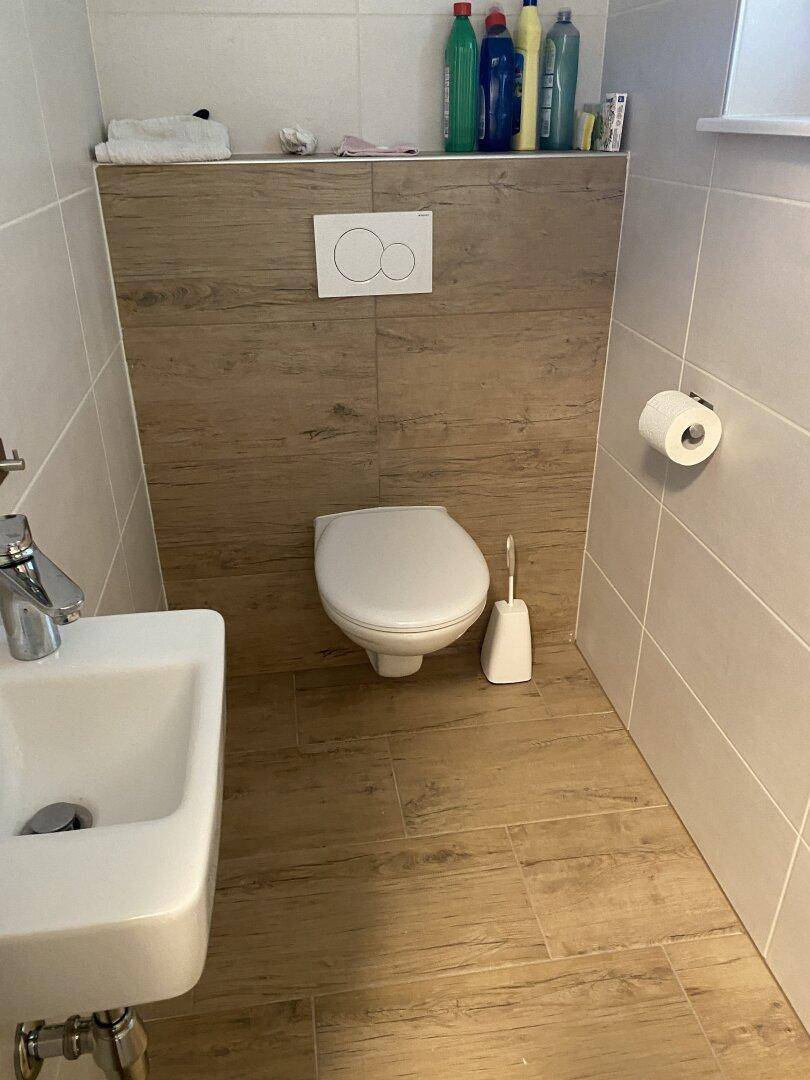 Kleines Gäste-WC mit modernem Design, wandhängendem WC und Holzoptik-Fliesen an Wand und Boden.