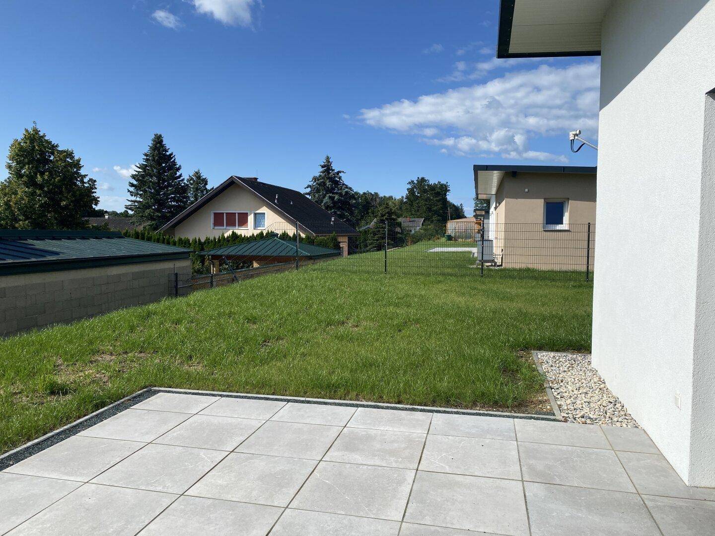 Neu angelegte Terrasse mit grauen Fliesen und Blick auf den frischen Rasen und die Nachbarschaftshäuser.