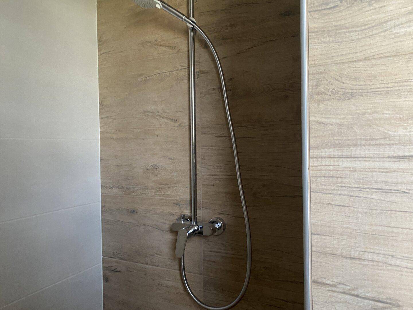 Duschbereich mit modernen Holzoptik-Fliesen an der Wand und einfacher Duscharmatur.