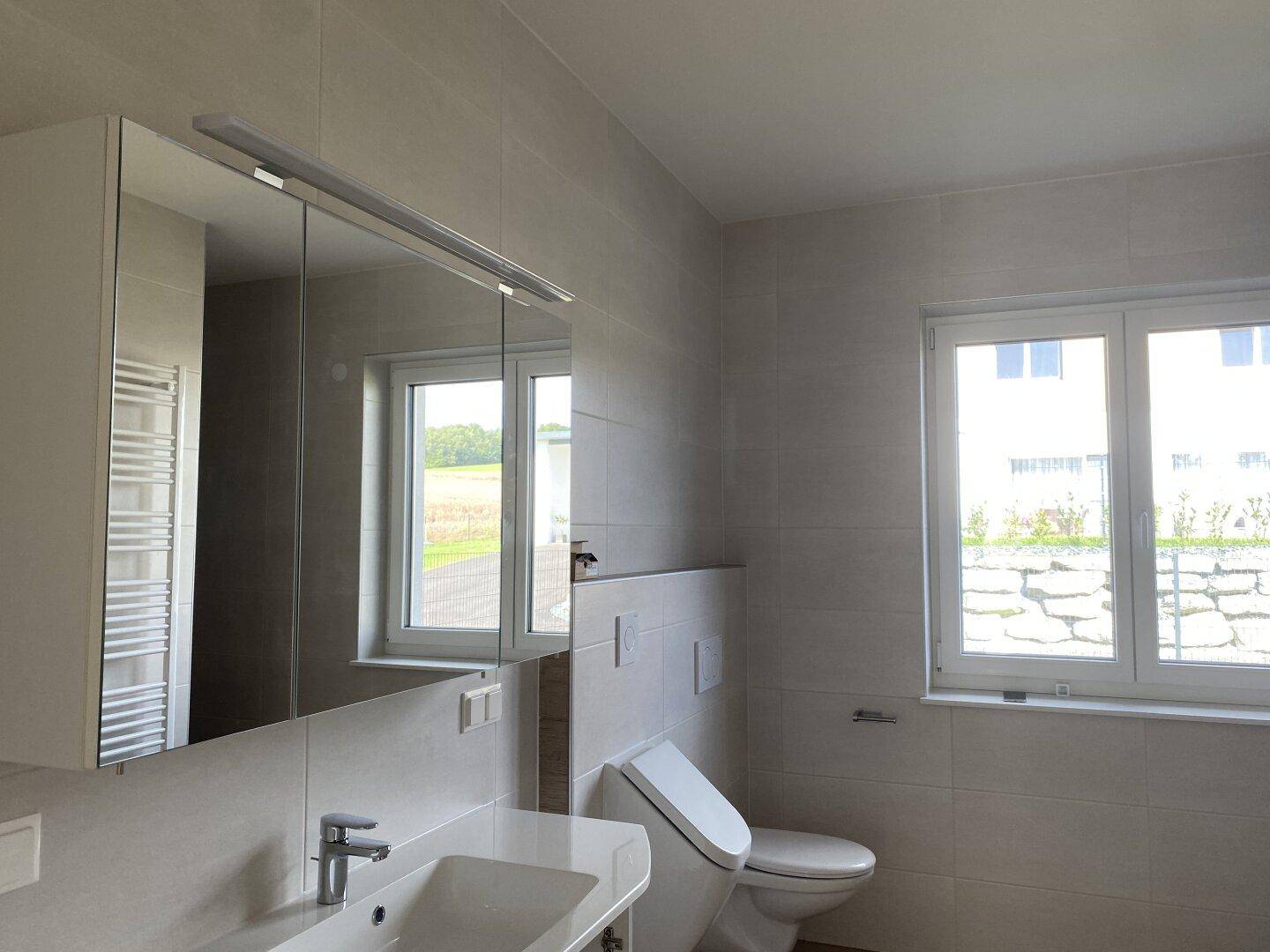 Modernes Badezimmer mit Einzelwaschbecken, Spiegelschrank, wandhängendem WC und Fenster.
