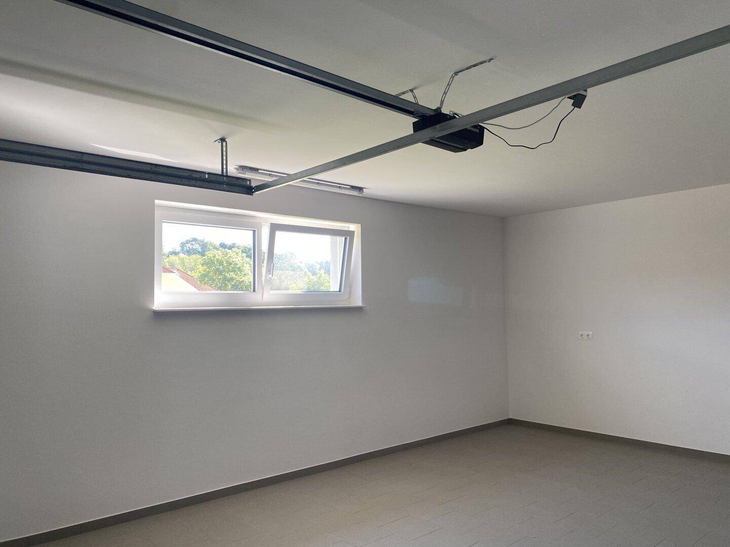 Geräumige Garage mit Fenster und automatischem Garagentoröffner-Mechanismus an der Decke.
