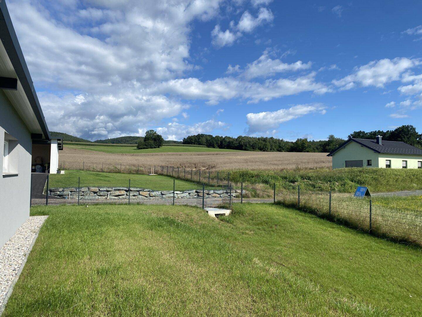 Weitläufiger Blick vom Grundstück über grüne Felder und sanfte Hügel in die umliegende Landschaft.