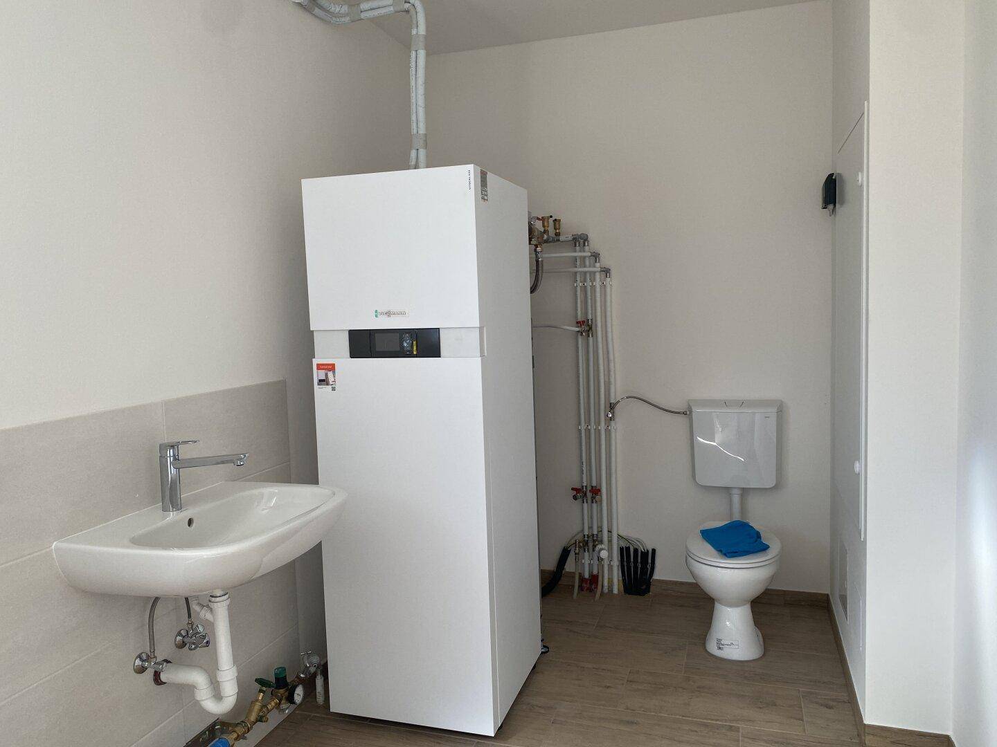 Technikraum mit Wärmepumpe, Waschbecken und WC, funktional und sauber gestaltet.