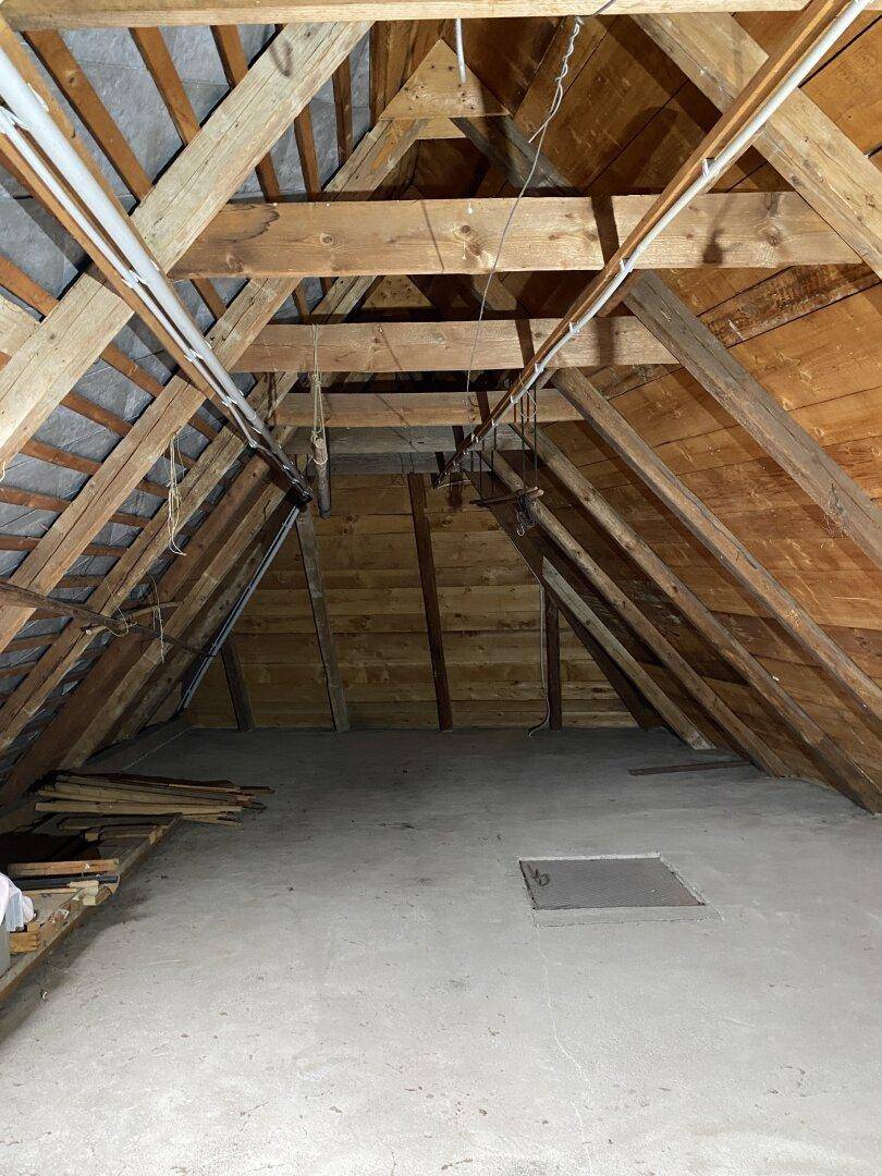 Unausgebauter Dachboden mit sichtbaren Holzbalken und Betonboden, bietet Ausbaupotenzial.
