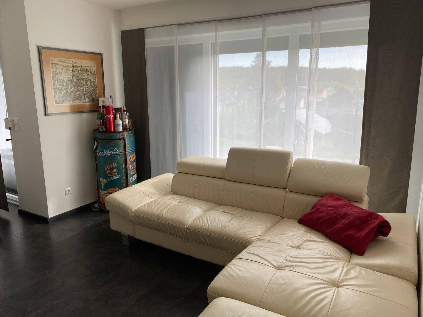Gemütliches Wohnzimmer mit großem Ecksofa und hellen Fenstern, die viel Tageslicht hereinlassen.