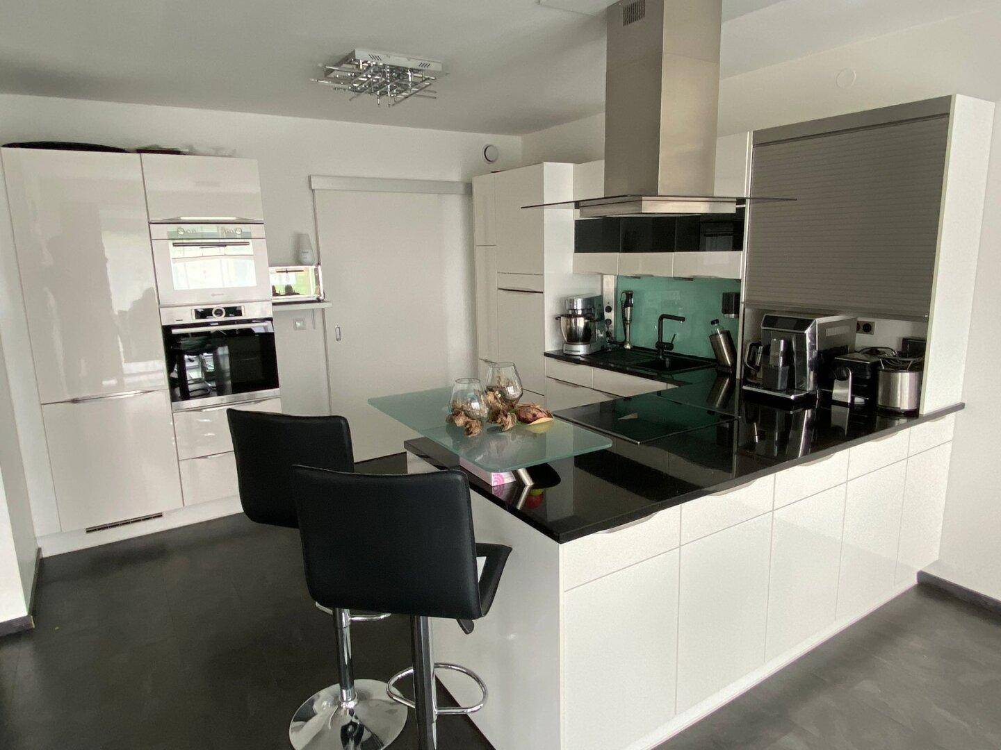 Moderne Küche mit weißen Hochglanzfronten, schwarzer Arbeitsplatte und einer Kücheninsel mit Frühstücksbar.