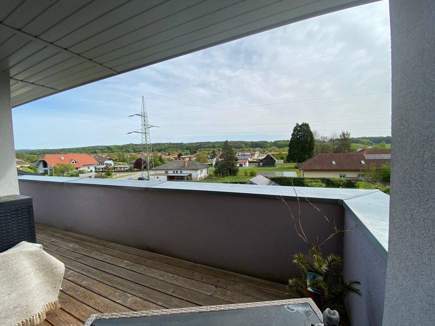 Geräumiger Balkon mit Holzboden und weitem Blick auf die grüne Umgebung und weitere Häuser.