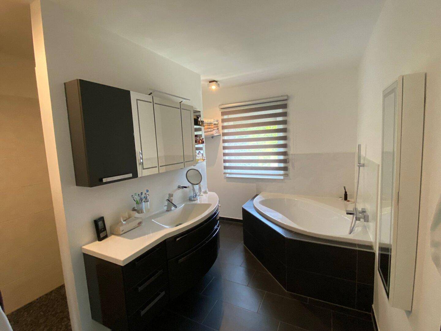Modernes Badezimmer mit Doppelwaschbecken, Eckbadewanne und einem Fenster für natürliche Belüftung.