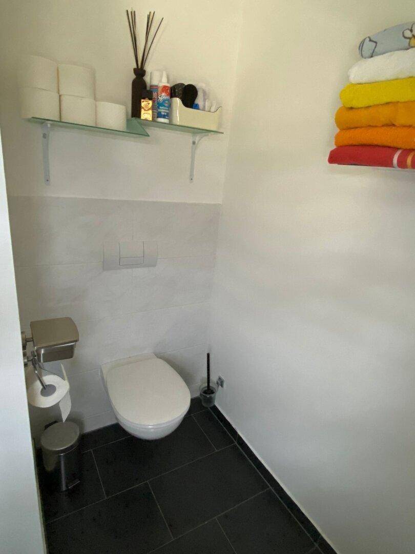 Weiteres Gäste-WC mit wandhängender Toilette und dunklen Bodenfliesen, schlicht und funktional.