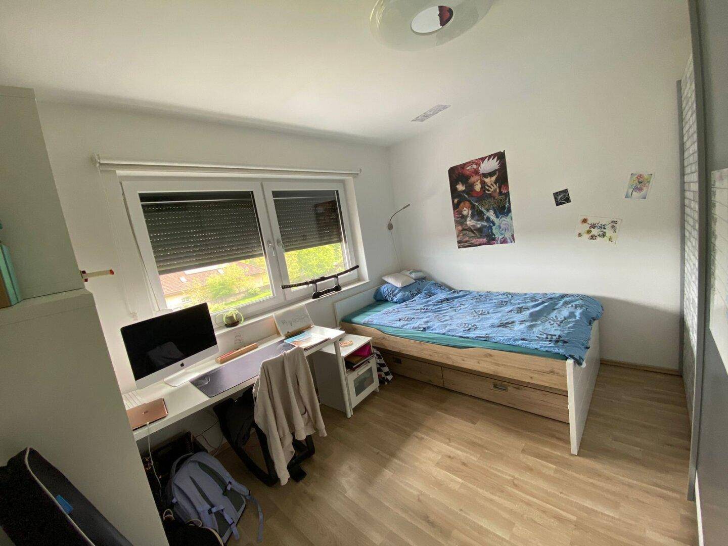 Helles Schlafzimmer mit Einzelbett, Schreibtisch und Fenster mit Rollläden, ideal für Kinder oder Gäste.