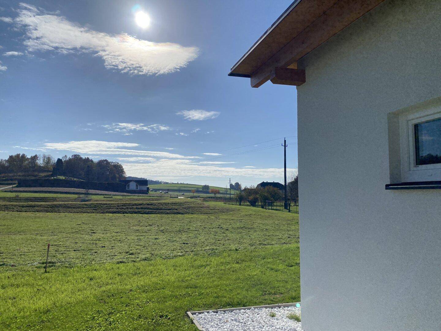 Sonniger Außenbereich des Hauses mit grünem Rasen und weitem Blick in die ländliche Umgebung.