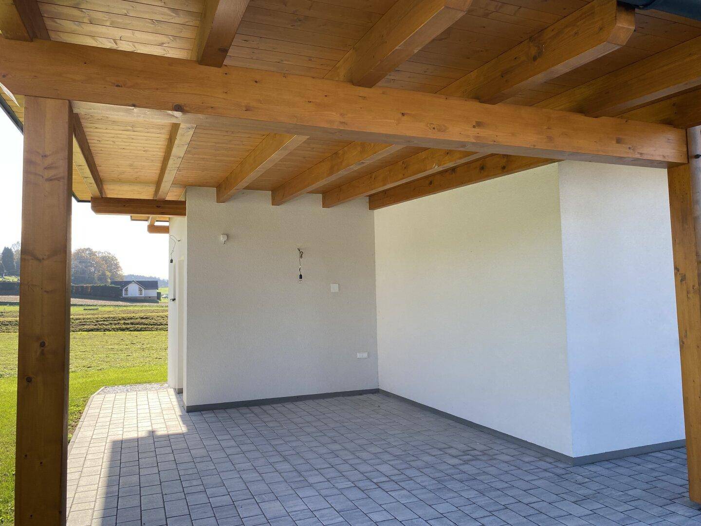 Überdachter Außenbereich mit sichtbaren Holzsparren und gefliestem Boden, ideal als Terrasse oder Carport.