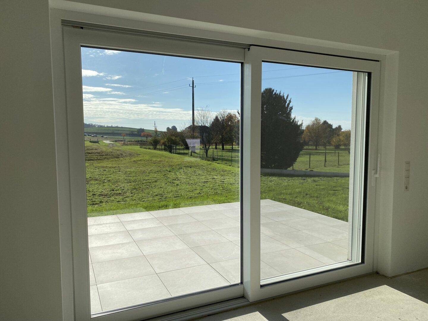 Große Glasschiebetür öffnet sich zu einer gefliesten Terrasse mit weitem Blick ins Grüne.
