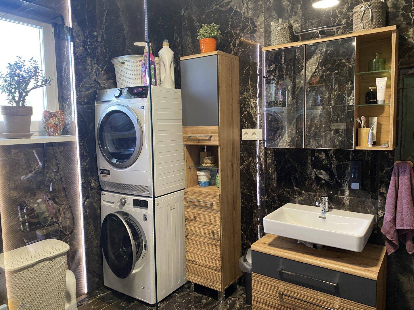 Modernes Badezimmer mit dunklen Marmorfliesen, Waschmaschine und Trockner.