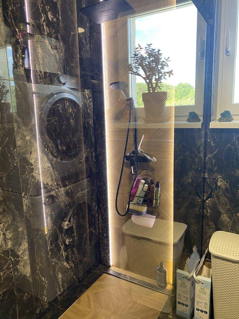 Elegante begehbare Dusche mit dunklen Marmorfliesen und Fenster für Tageslicht.