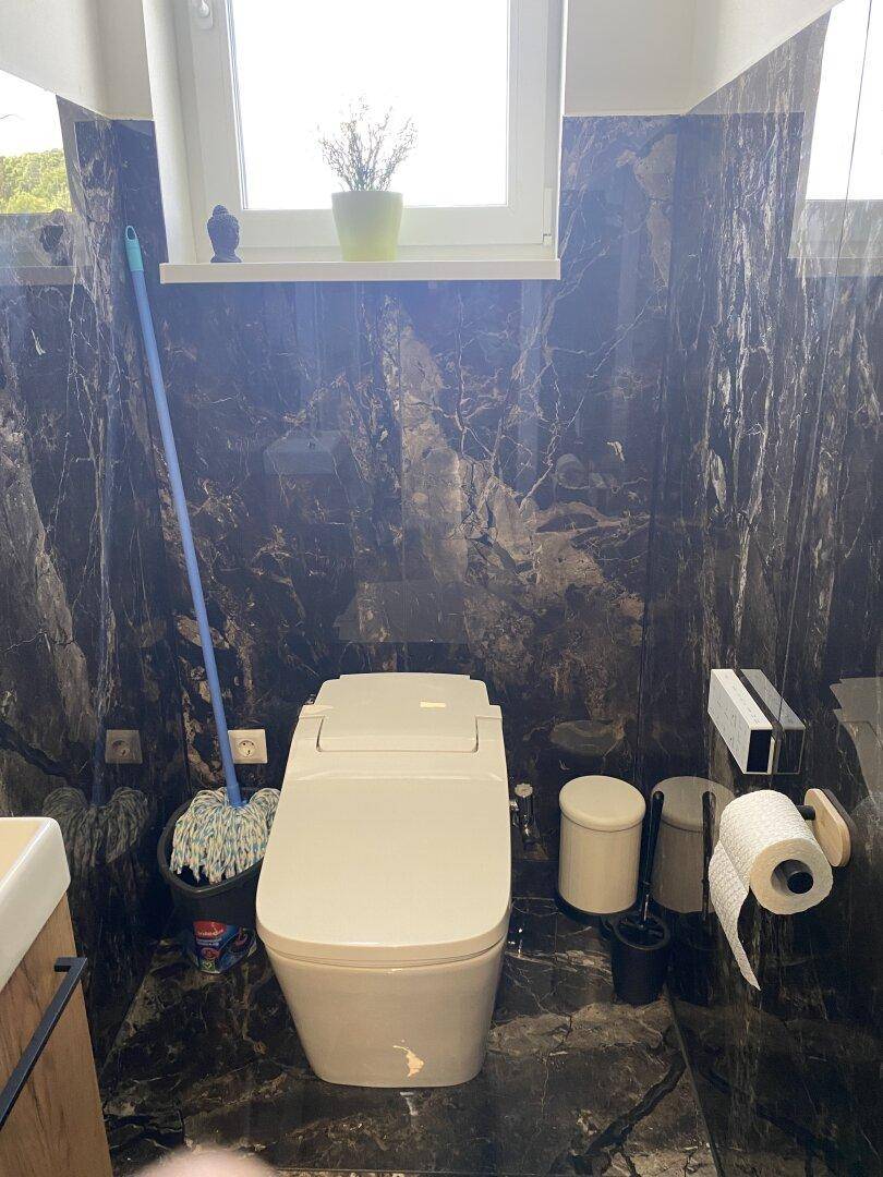 Modernes WC mit dunklen Marmorfliesen und Fenster für natürliche Belüftung.