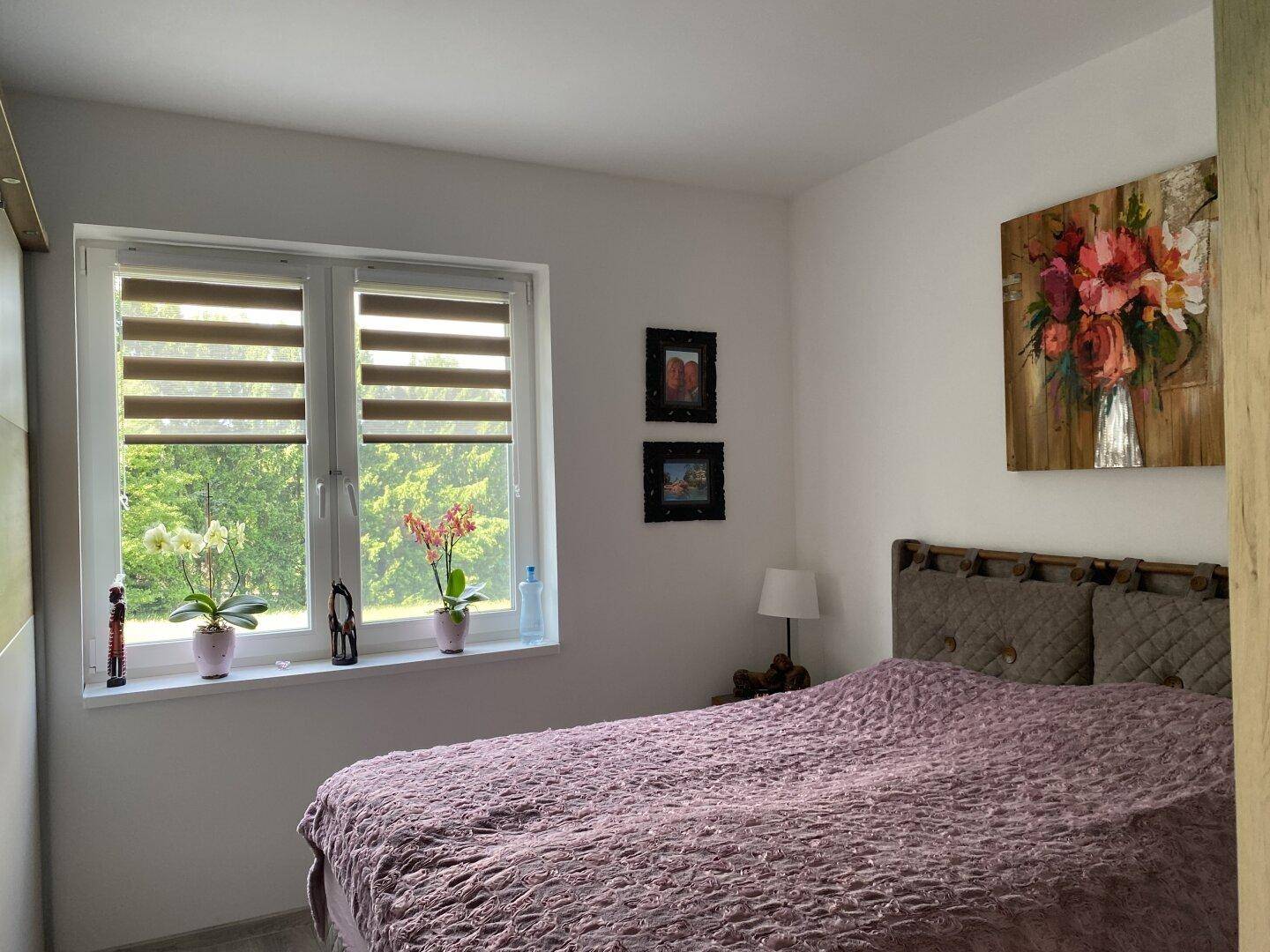 Ruhiges Schlafzimmer mit Doppelbett, farbenfrohem Bild und Fenster mit Blick ins Grüne.