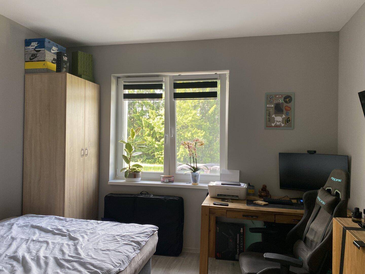 Helles Schlafzimmer mit Schrank, Schreibtisch und Fenster mit Blick ins Grüne.