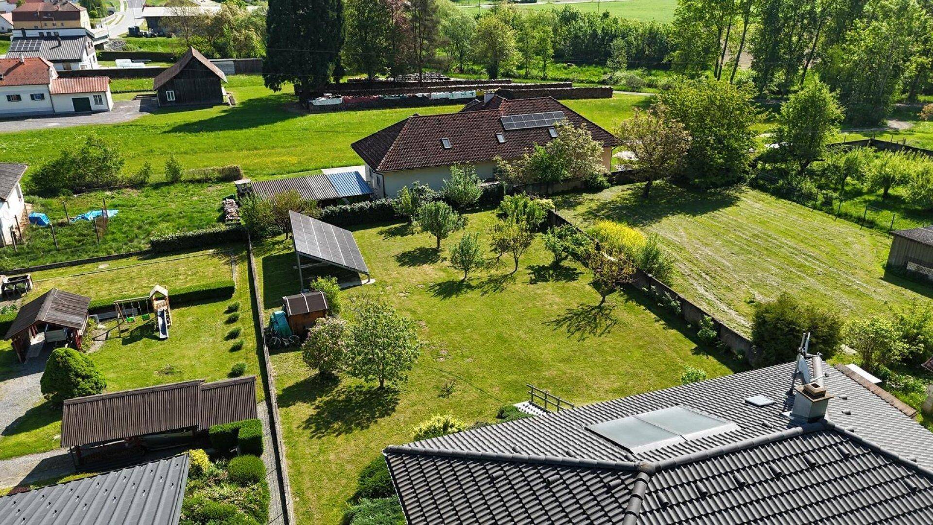 Weitläufige Luftaufnahme der ländlichen Umgebung mit Häusern, grünen Feldern und einer Photovoltaikanlage.