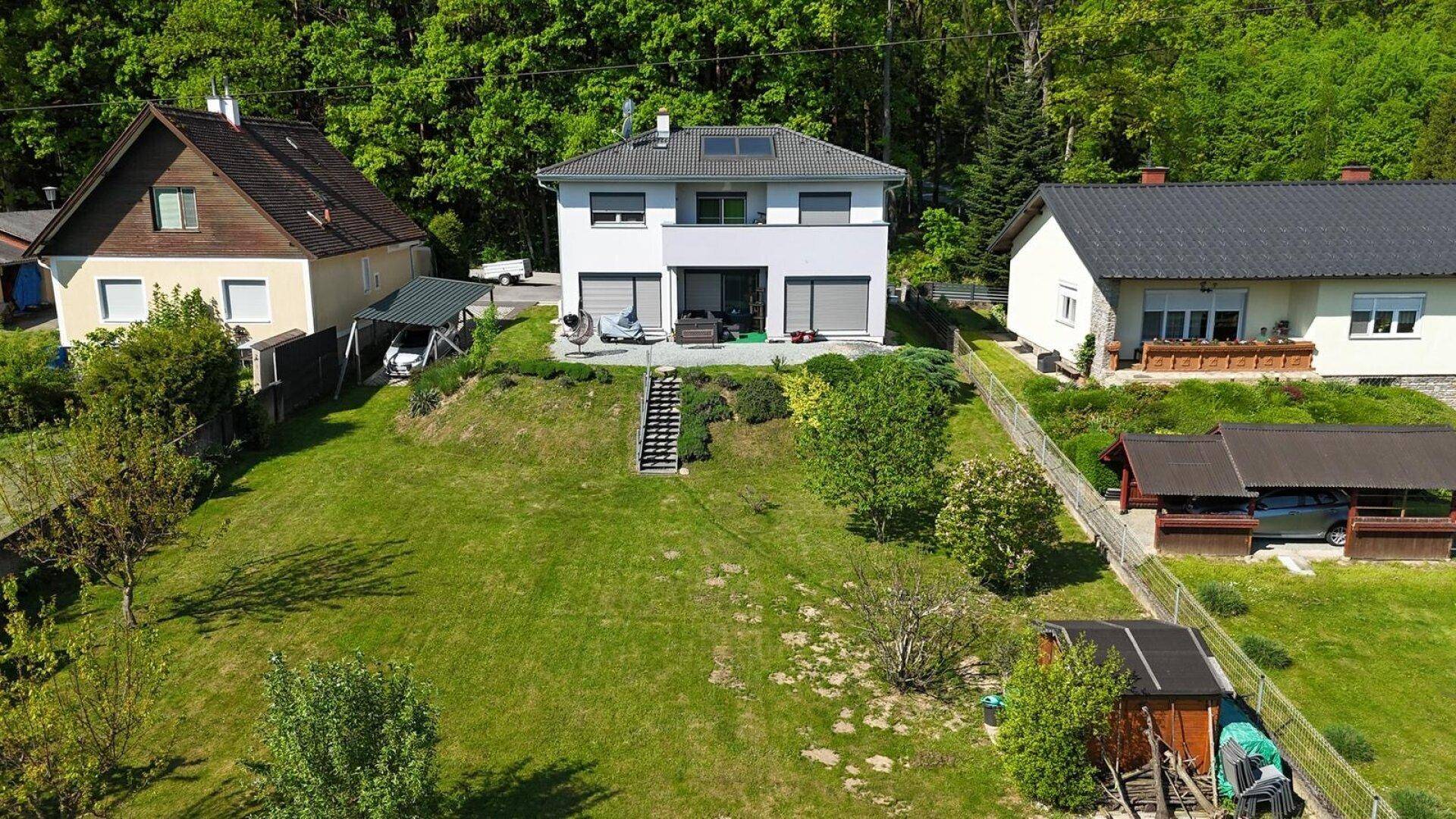 Weitläufiger Gartenbereich mit Rasenfläche und Treppe, umgeben von weiteren Häusern und viel Natur.
