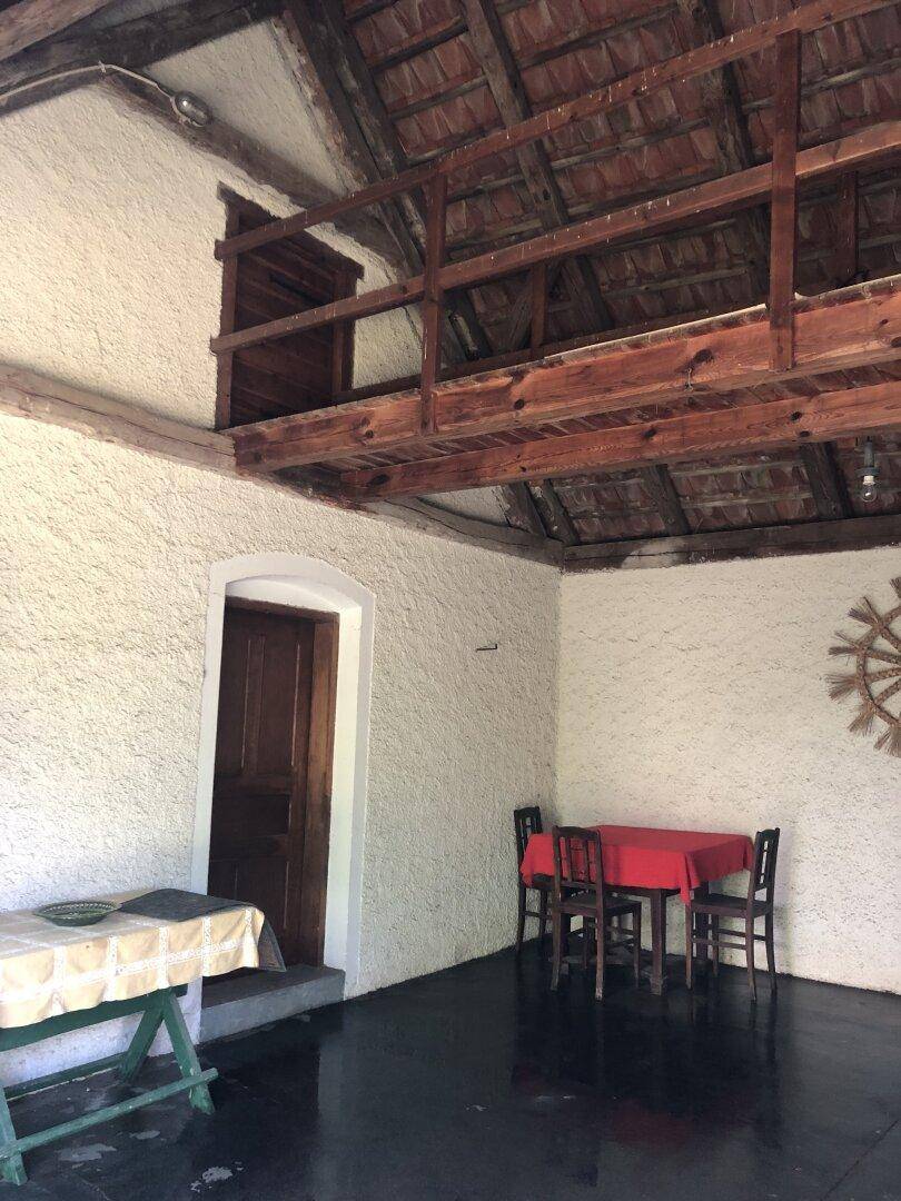 Rustikaler überdachter Bereich mit Holzbalkendecke und einfacher Sitzgelegenheit.