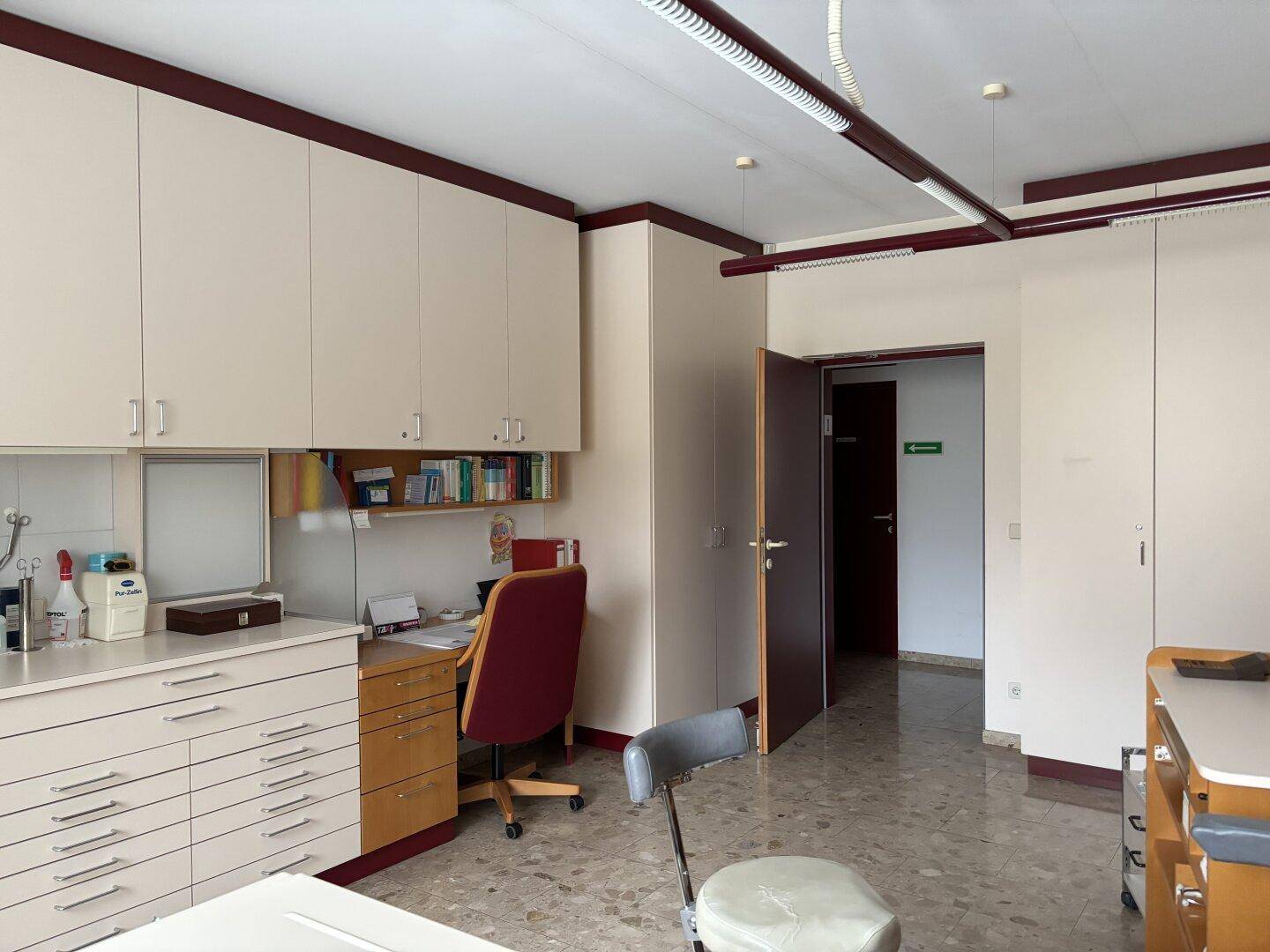 Büro oder Sprechzimmer mit Einbauschränken, Schreibtisch und gefliestem Boden.