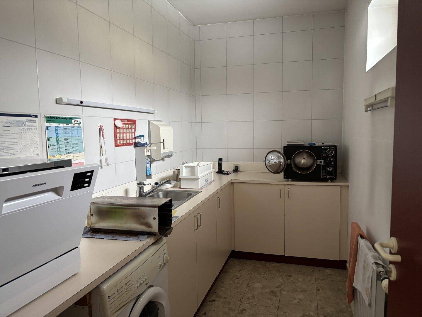 Funktionsraum mit Spülbecken, Arbeitsplatte, Waschmaschine und gefliesten Wänden.