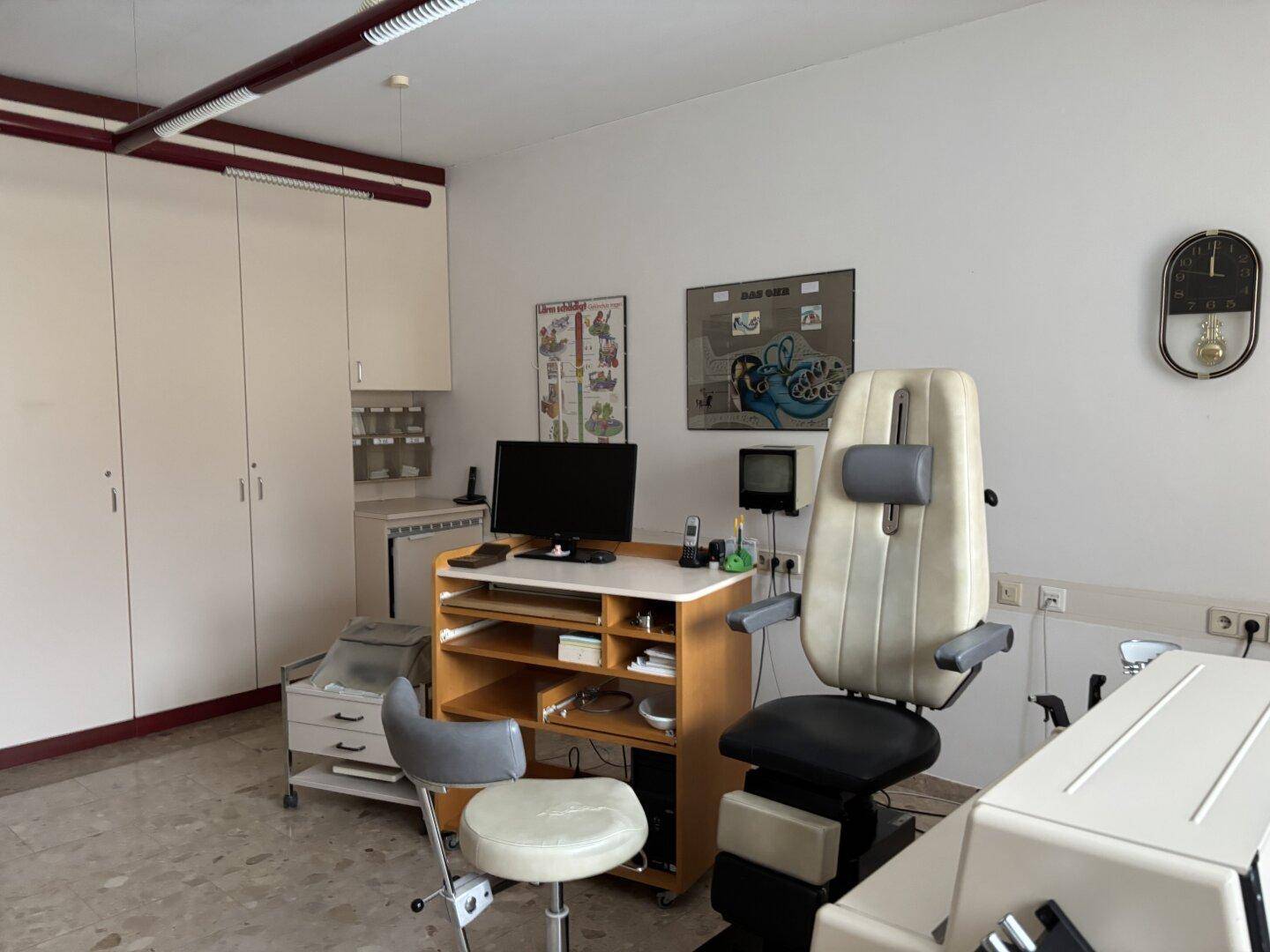 Behandlungszimmer mit medizinischen Geräten, Schreibtisch und Einbauschränken.