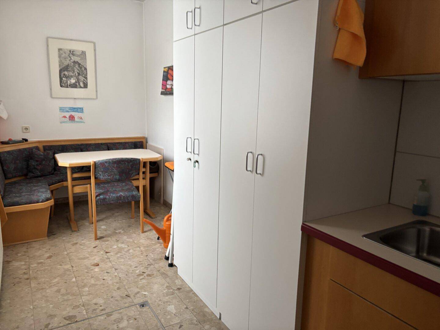 Kleine Teeküche oder Pausenraum mit Sitzecke, Schränken und Spülbecken.