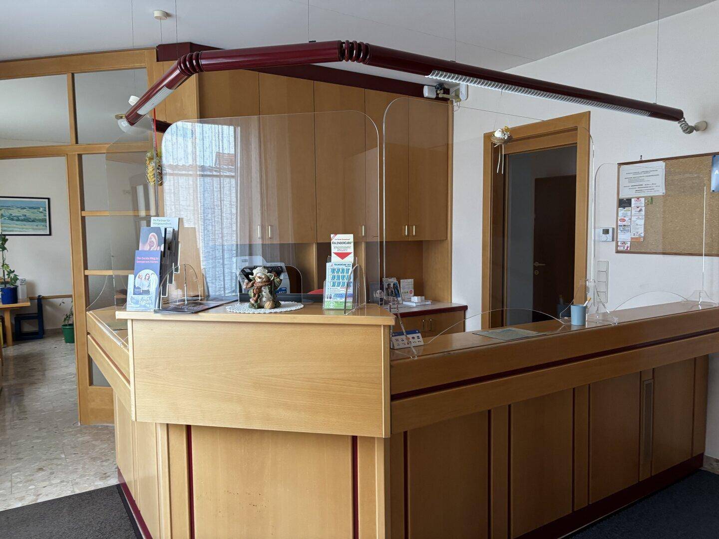 Empfangsbereich mit hölzerner Theke, Plexiglasschutz und Blick in angrenzende Räume.
