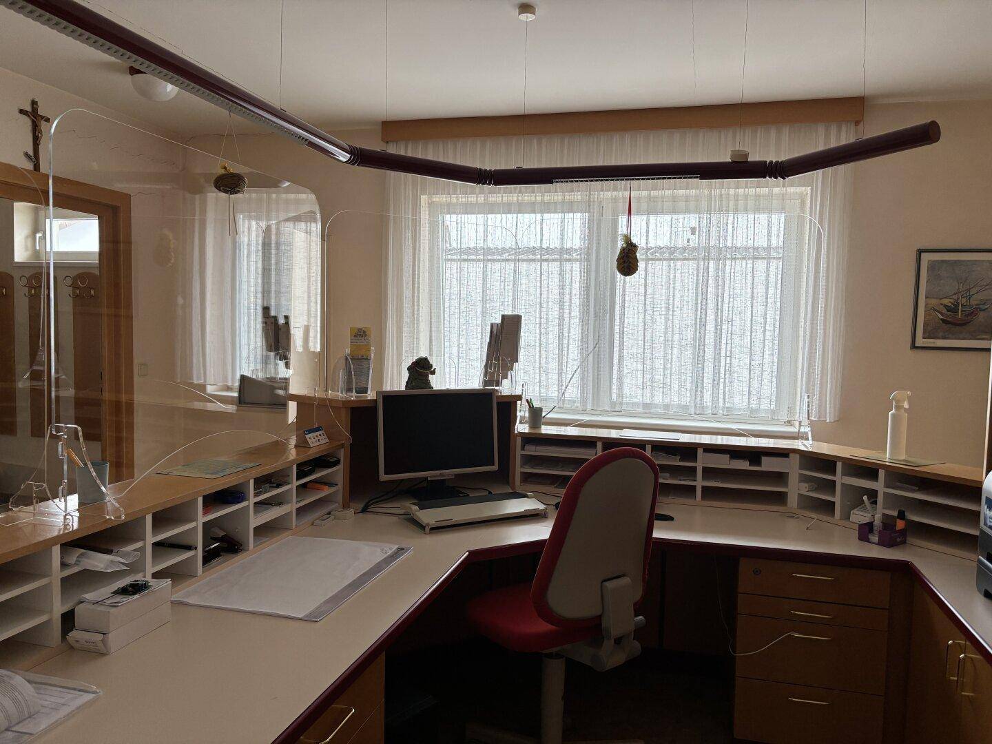 Arbeitsplatz am Empfang mit Computer, Bürostuhl und großem Fenster mit Vorhängen für Tageslicht.