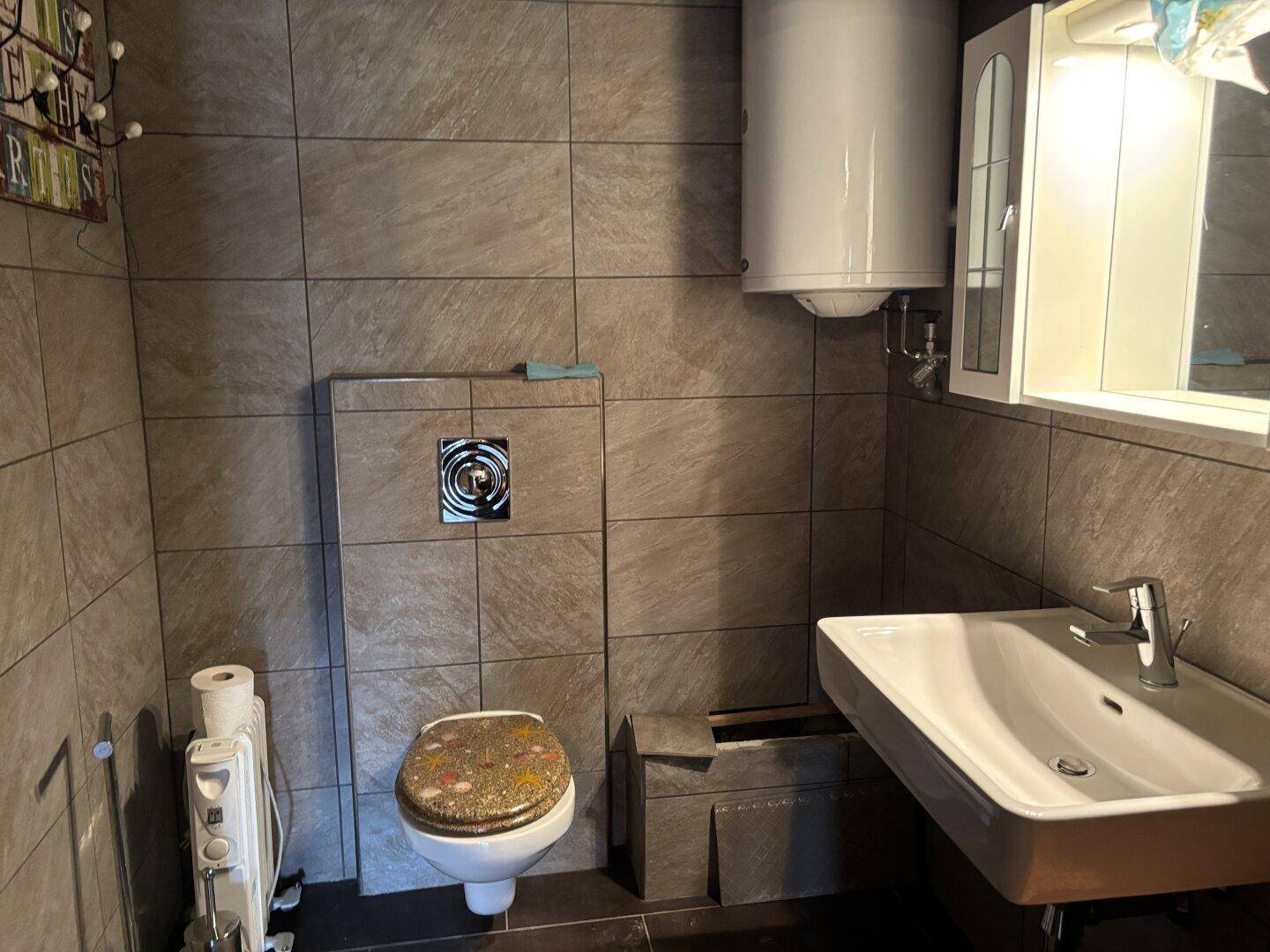 Kleines Badezimmer mit grauen Fliesen, Toilette und Waschbecken.