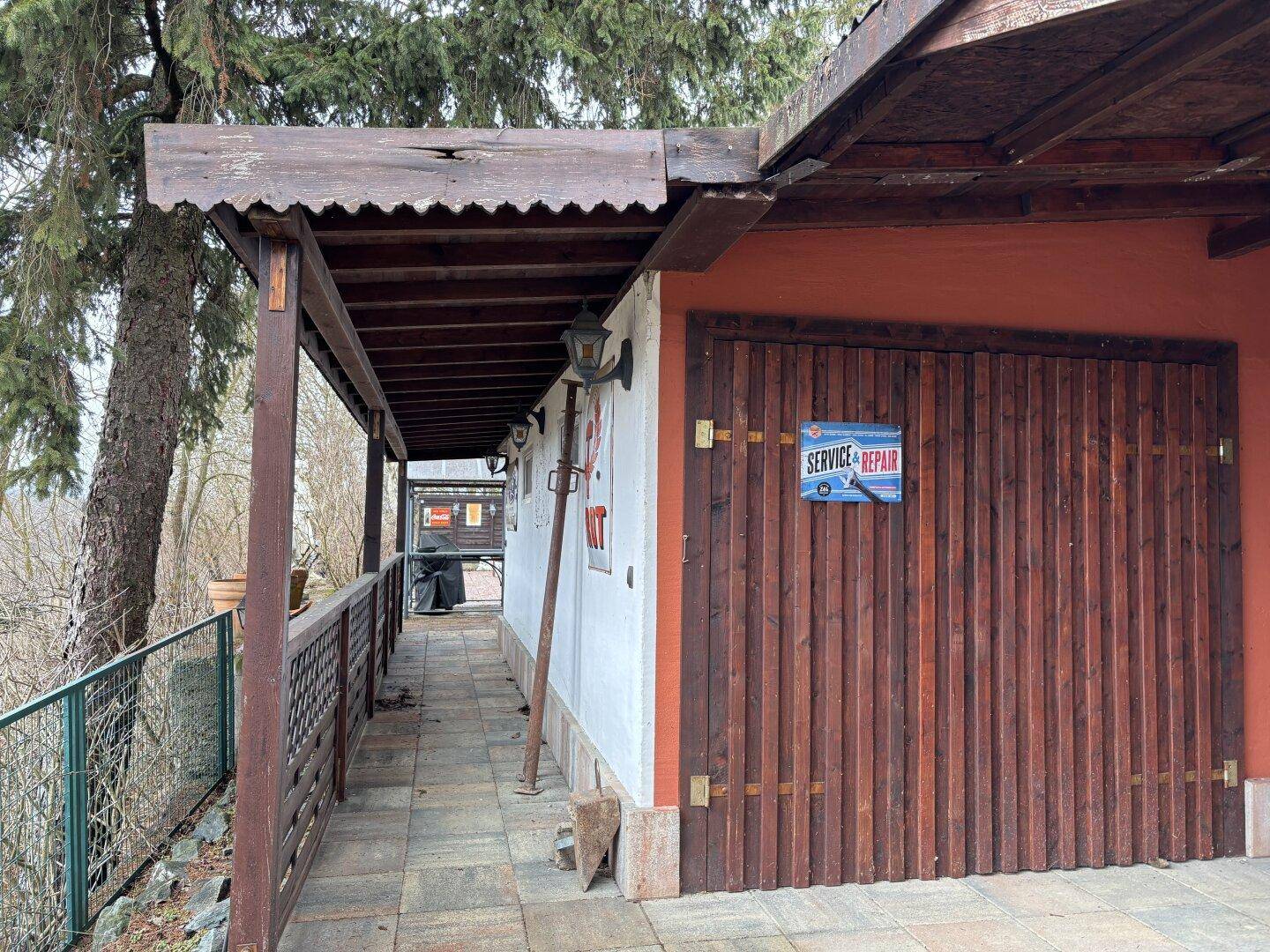 Überdachter Gangbereich mit Holzbalken und Zugang zu einer Holzgarage.
