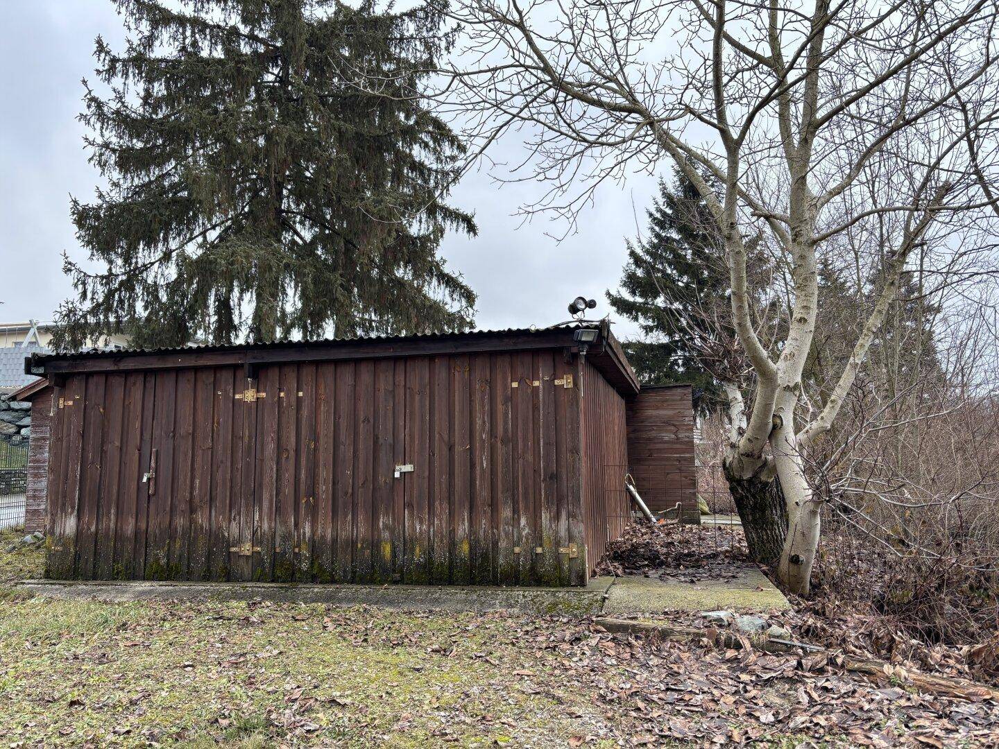 Rustikaler Holzschuppen im Gartenbereich, umgeben von Bäumen.
