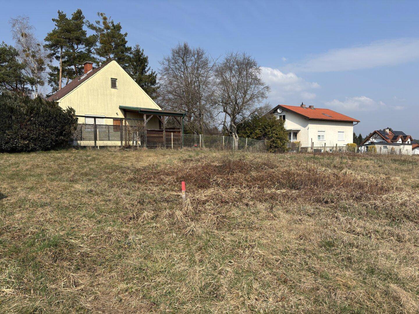 Haus mit gelber Fassade und rotem Dach, umgeben von trockenem Gras und Bäumen.