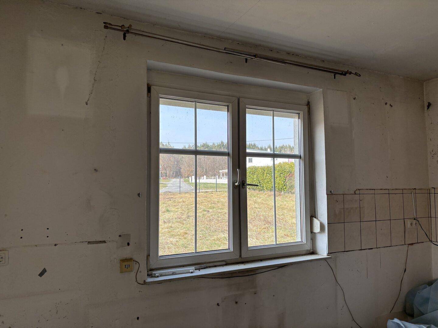 Renovierungsbedürftiger Raum mit einem Fenster und teilweise gefliesten Wänden.