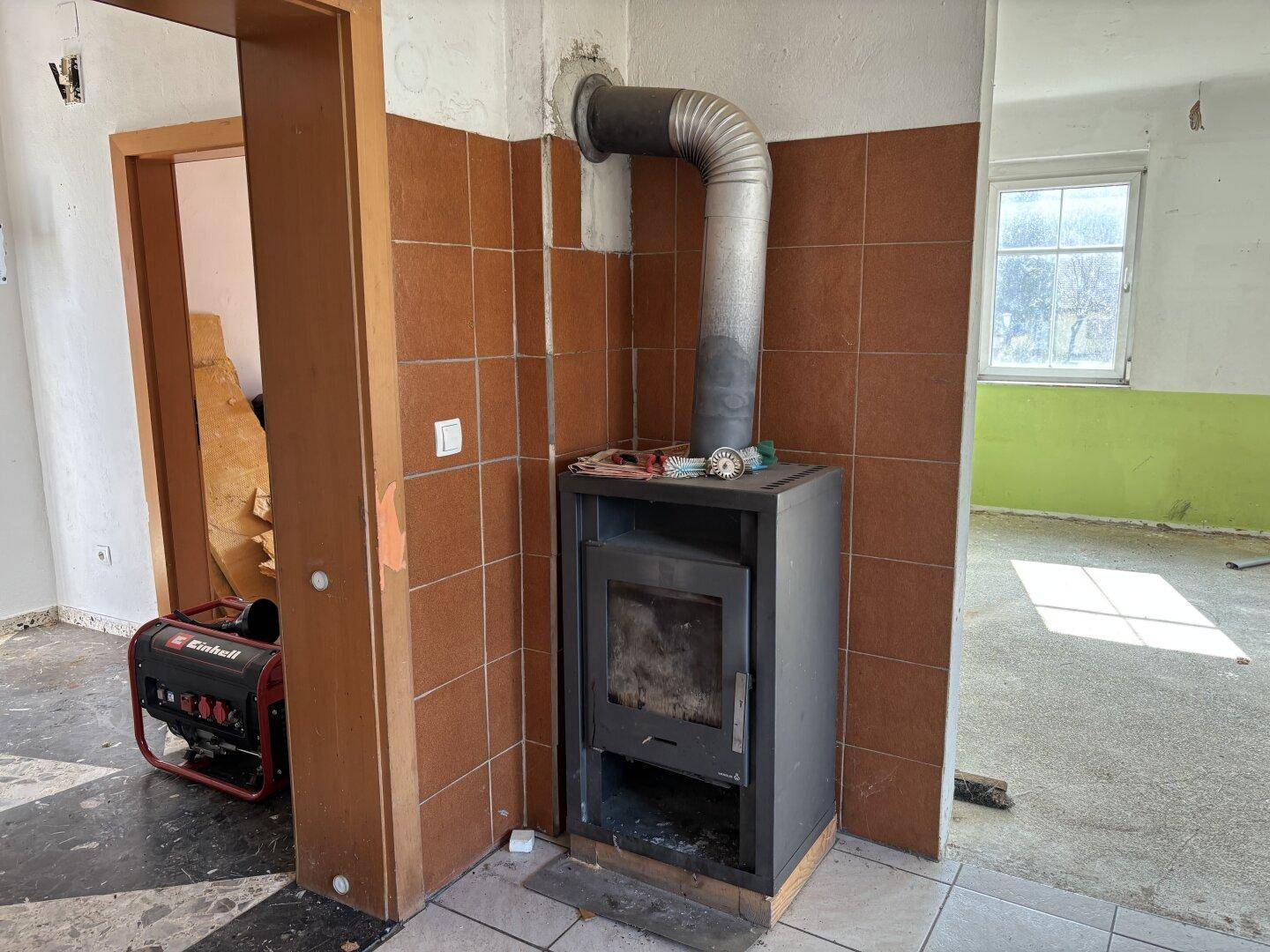 Wohnbereich mit einem Holzofen, braunen Wandfliesen und einem Generator im Hintergrund.